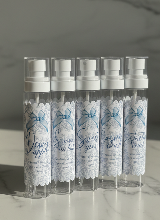 Set of six small spray bottles with decorative labels on a marble surface.